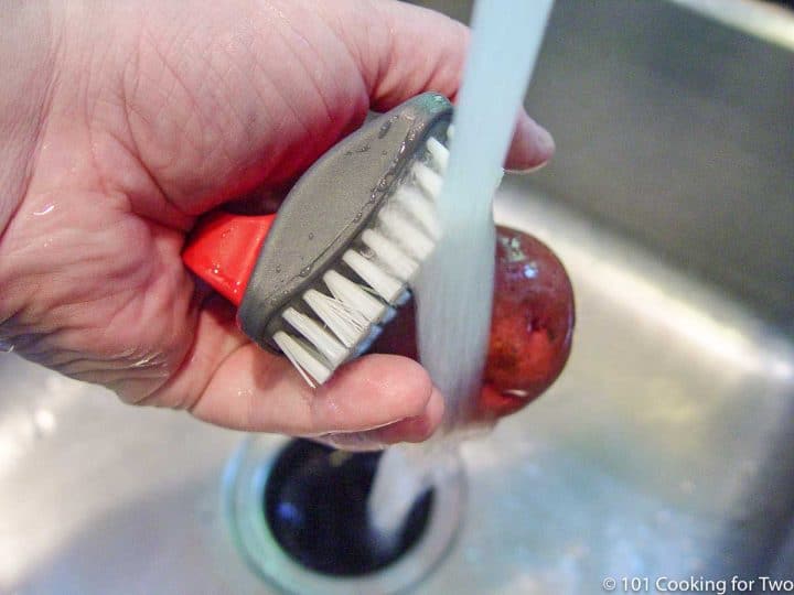 scrubbing a red potato under running water