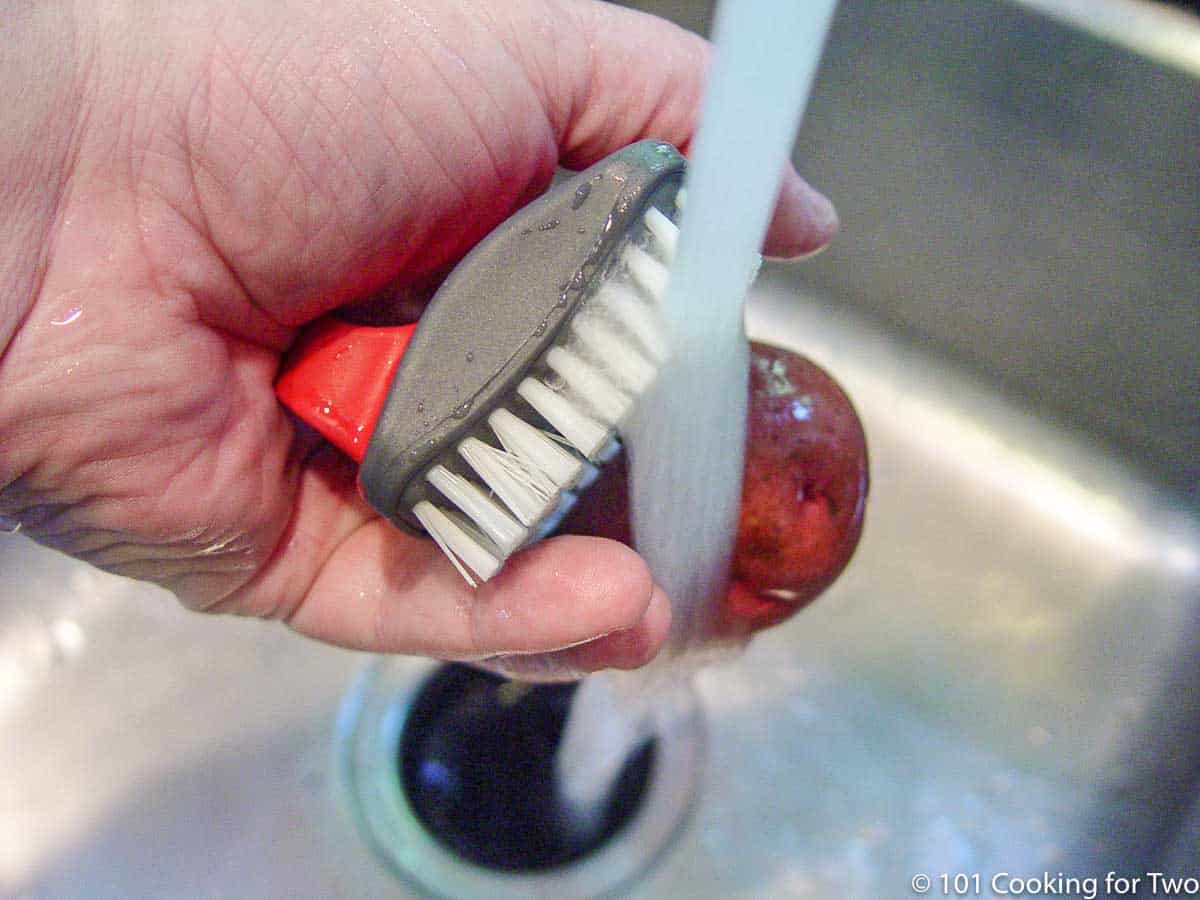 scrubbing a red potato under running water.