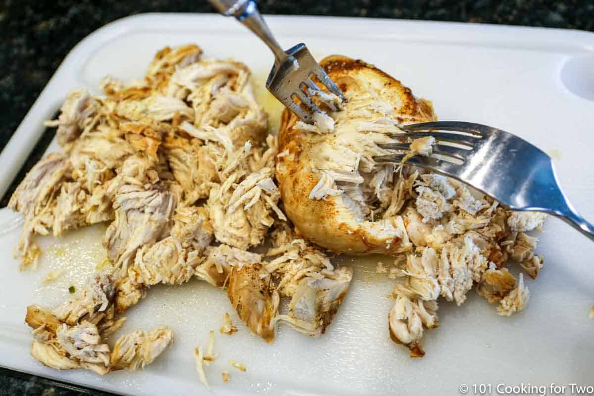 shredding cooked chicken on a white board