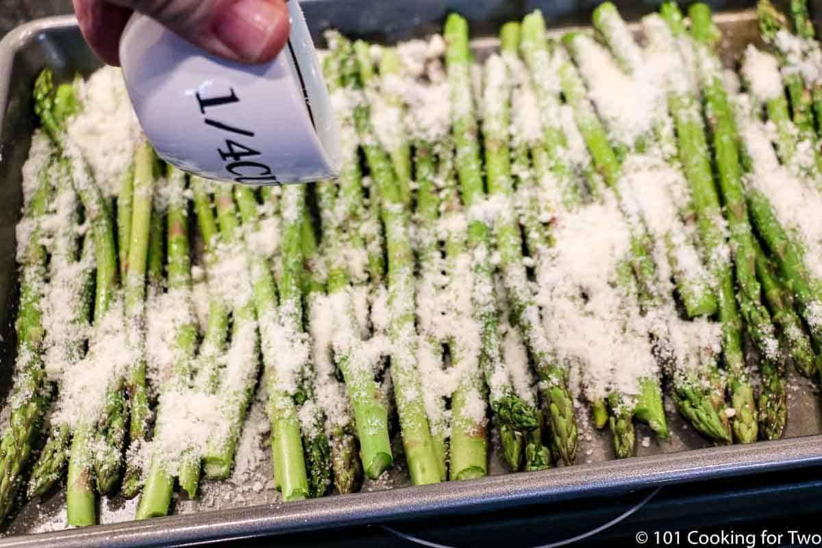 spreading Parmesan cheese on the asparagus.
