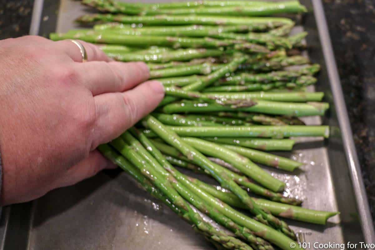 spreading asparagus on an oil coated tray.
