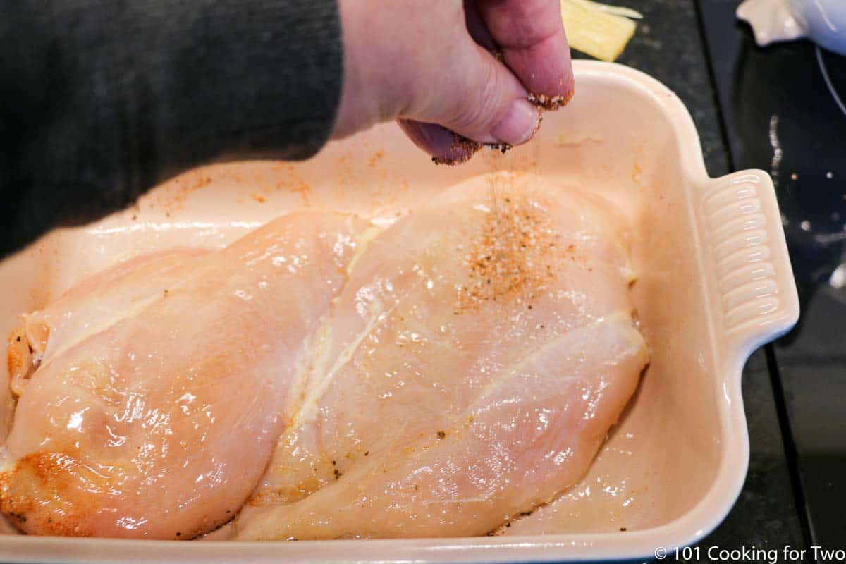 sprinkling chicken in the baking dish with spices