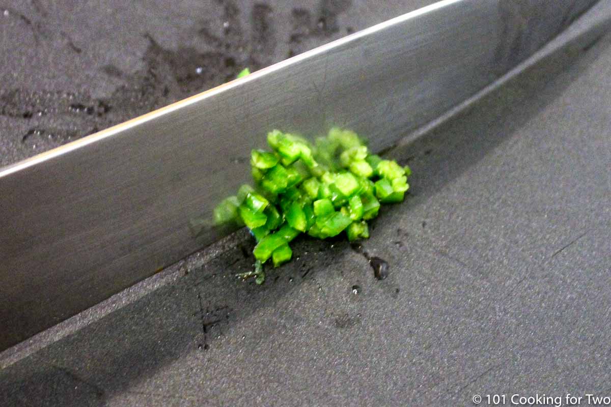 chopping a jalapeno on a black board.