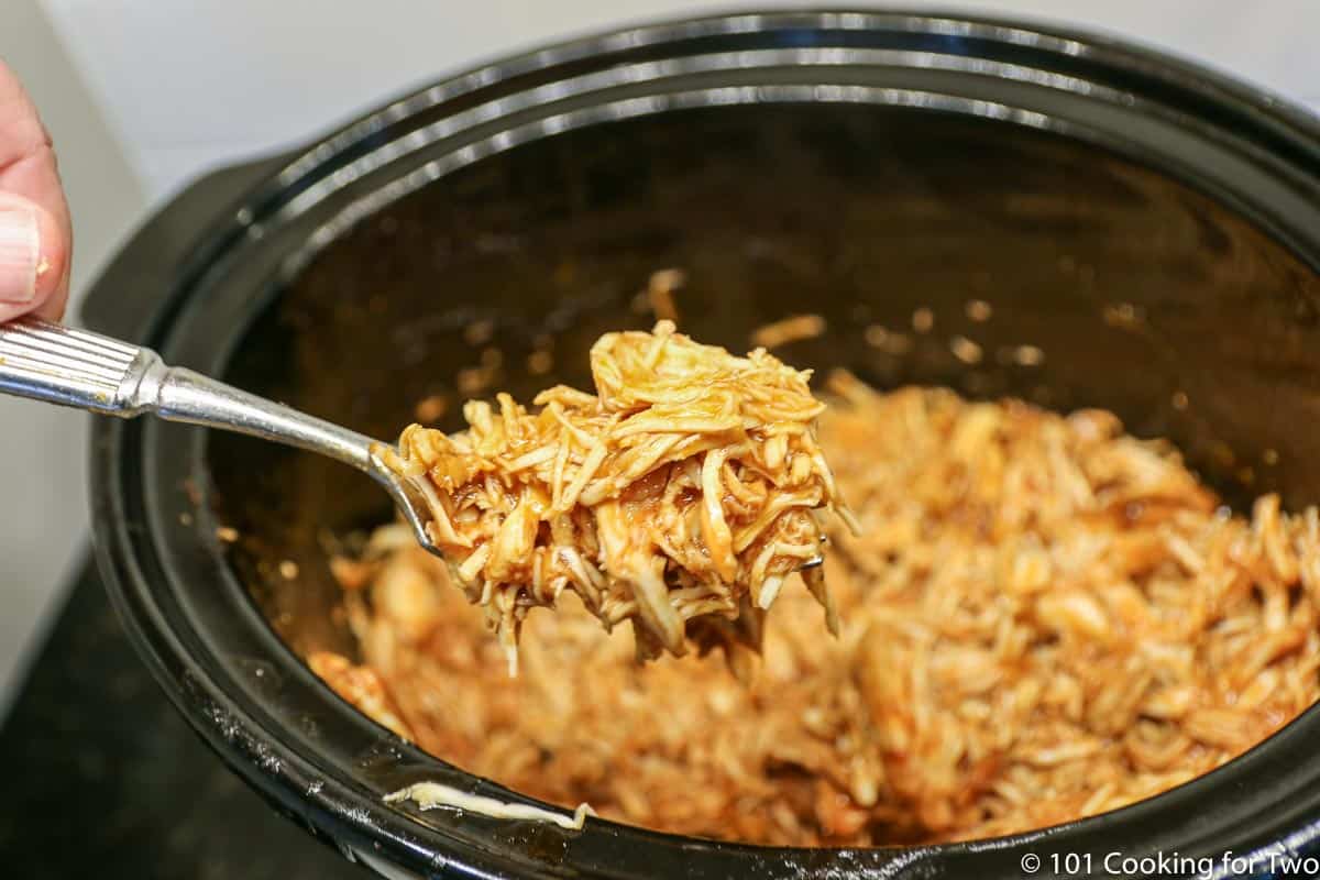 shredded BBQ chicken in a spoon over the crock pot