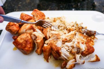 shredding cooked chicken with forks on a white board