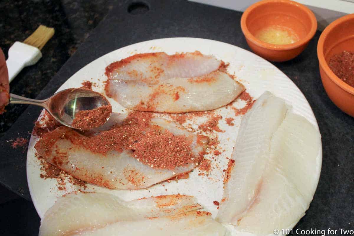adding spices to fish on white plate.