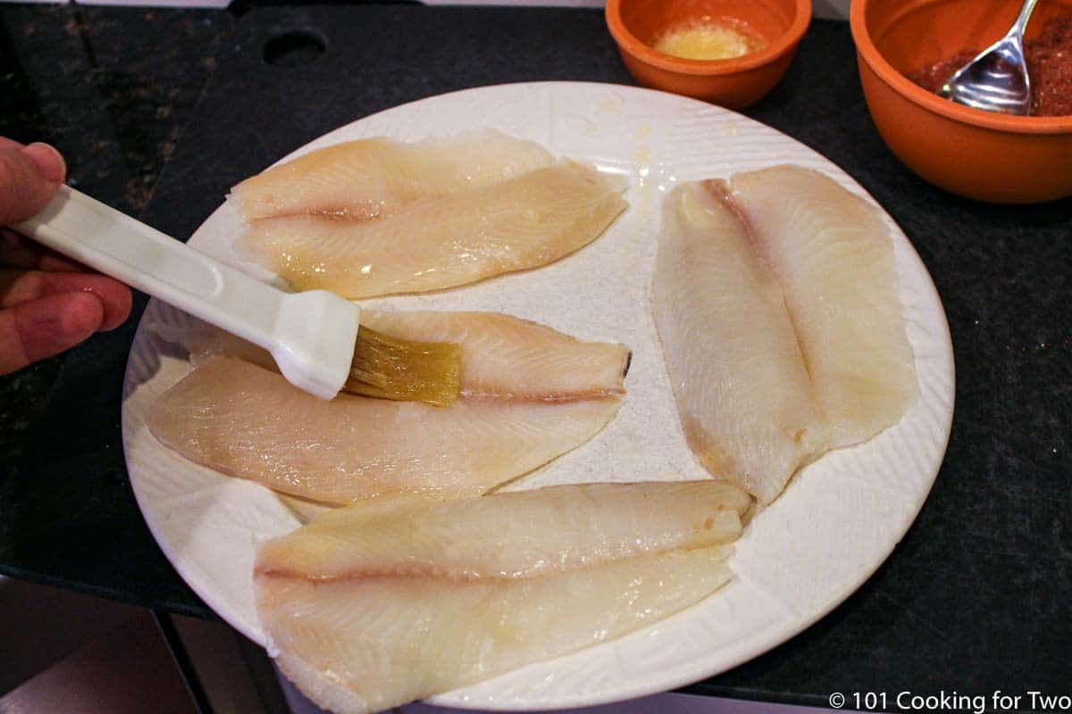 brushing fish with butter on a white plate