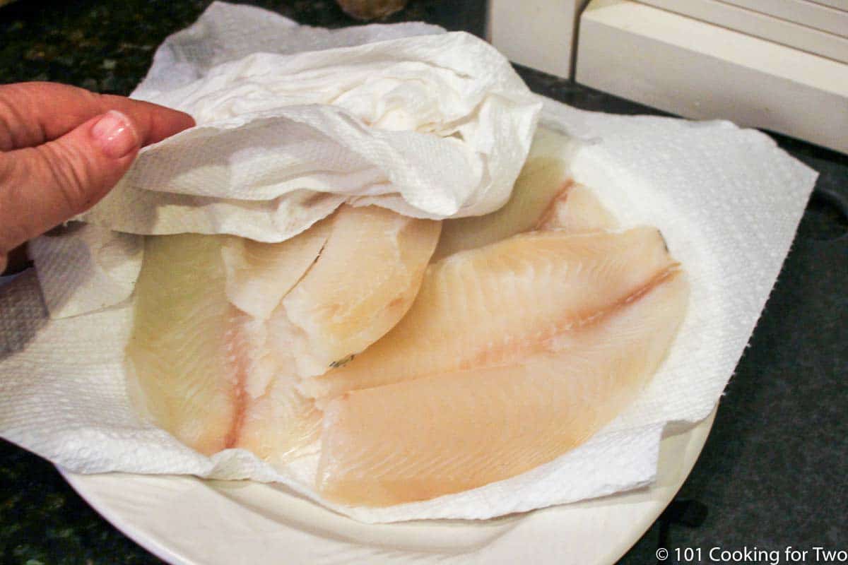 patting dry tilapia with paper towels.