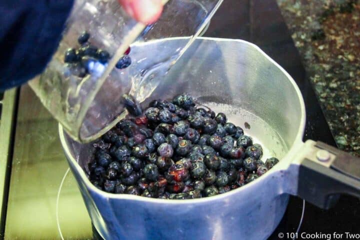 pouring blueberrins into sauce pan with sugar.