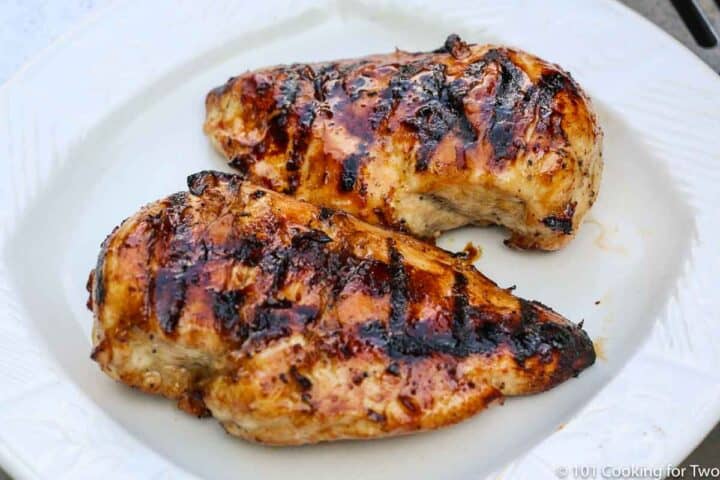two honey glazed chicken breasts on a white plate.
