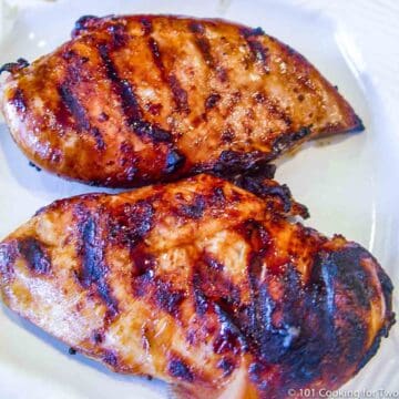 two marinaded grilled chicken on a whit plate.