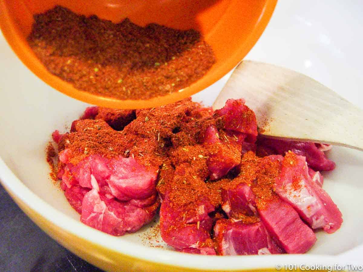 adding spices to bowl with cut up pork.