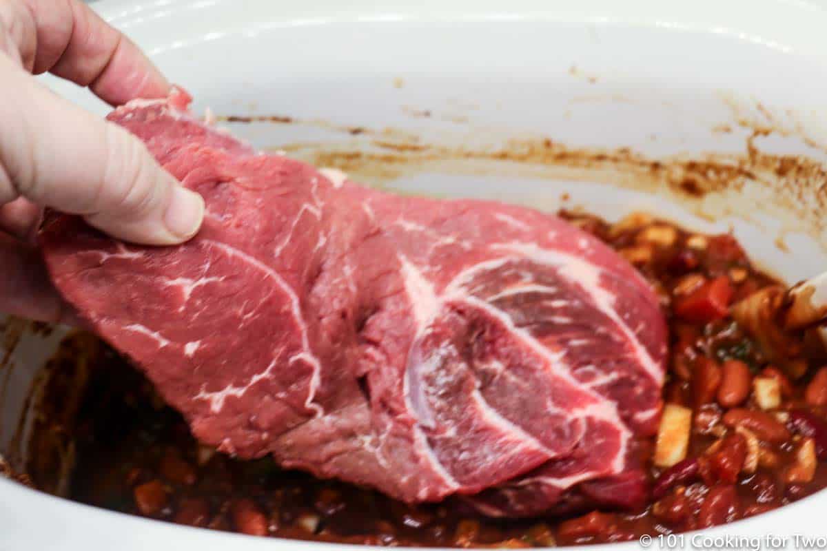 adding trimmed chuck roast to the crock pot.