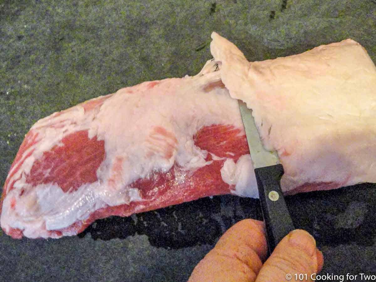cutting fat pad off boneless pork ribs.