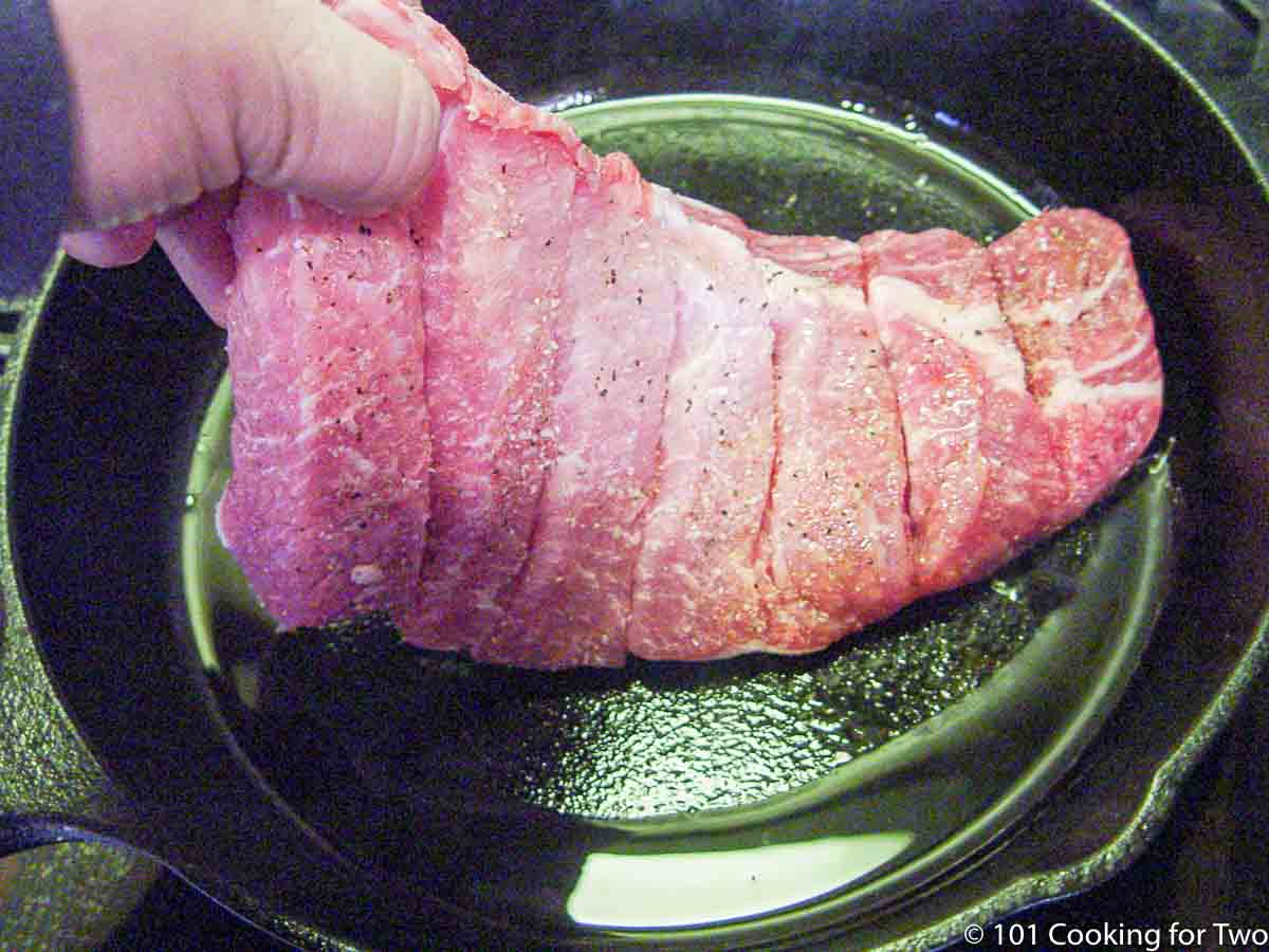 laying seasoned boneless ribs into preheated cast iron skillet.