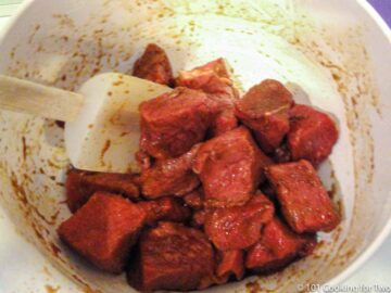 mixing sirloin steak with marinade in white bowl