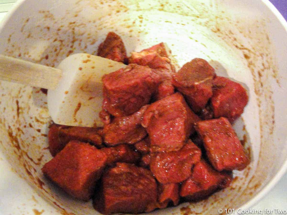 mixing sirloin steak with marinade in white bowl.