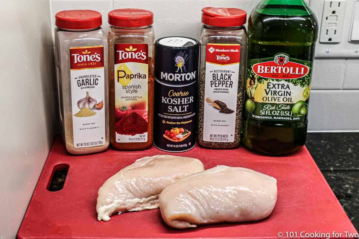 raw chicken breast with spices and oil on red board.