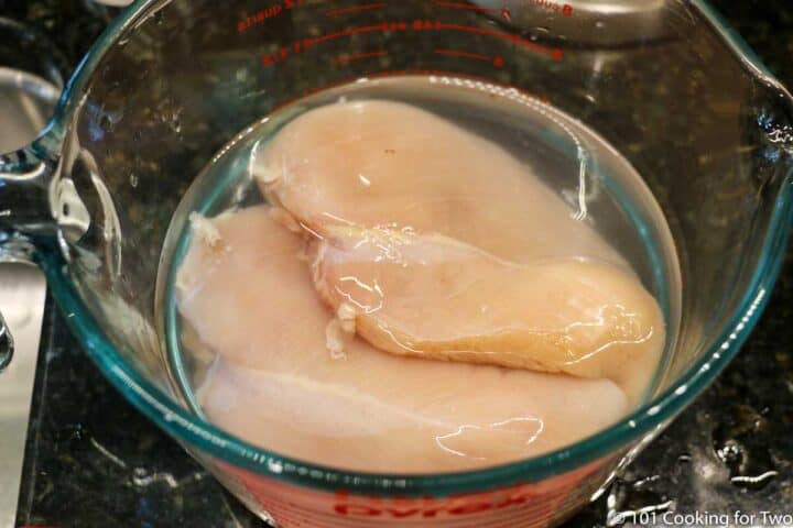 raw chicken breasts brining in a bowl.