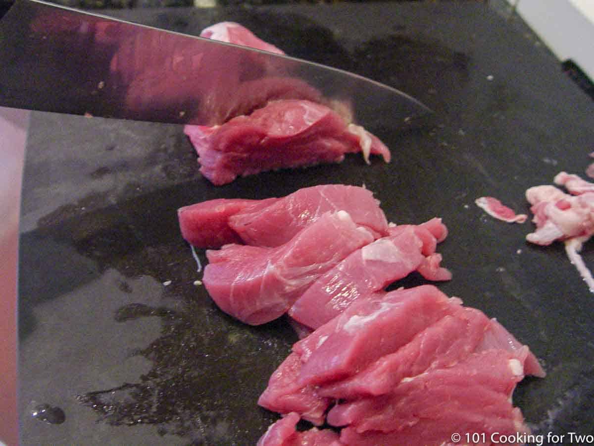 trimming a pork tenderloin on a black board.