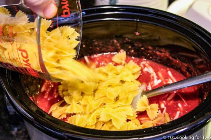 adding pasta to crock pot with sauce