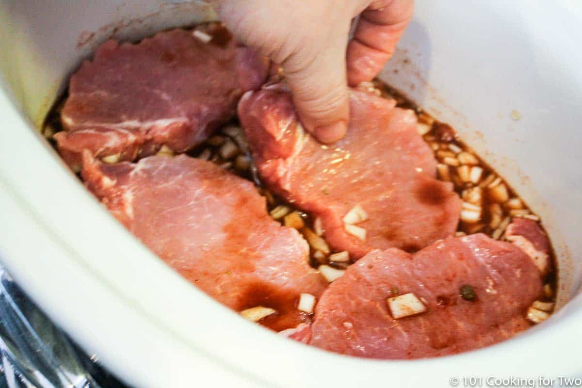 adding pork loin slices to the crock pot.