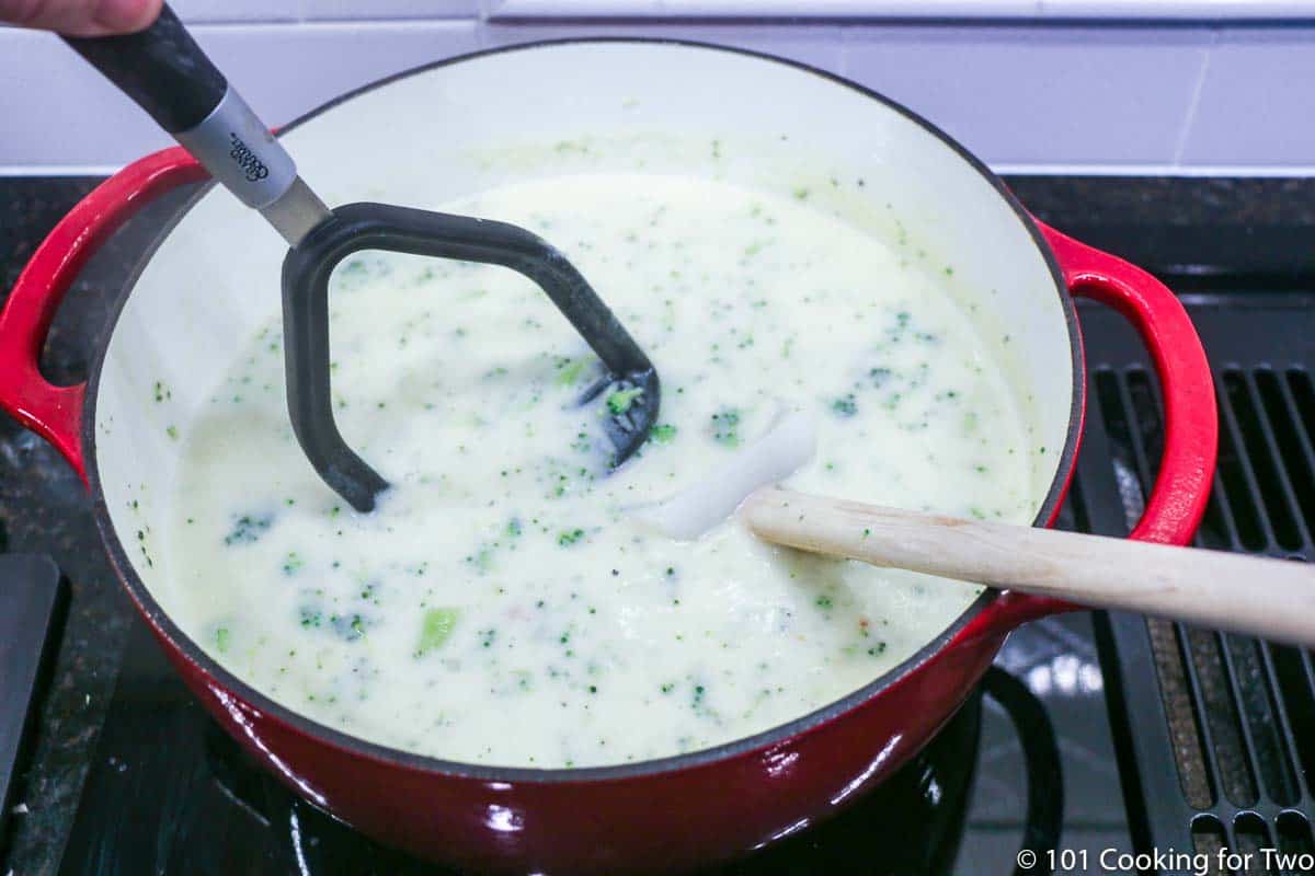 using a potato masher on the soup.