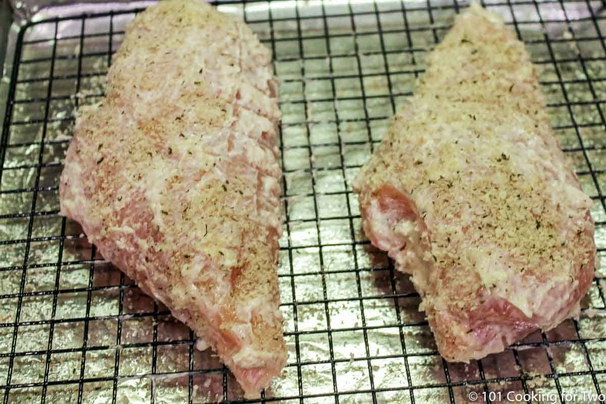 a light coat of bread crumbs on chicken breasts on a rack.