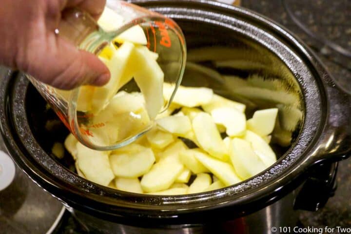 adding apple slices to prepared crock pot