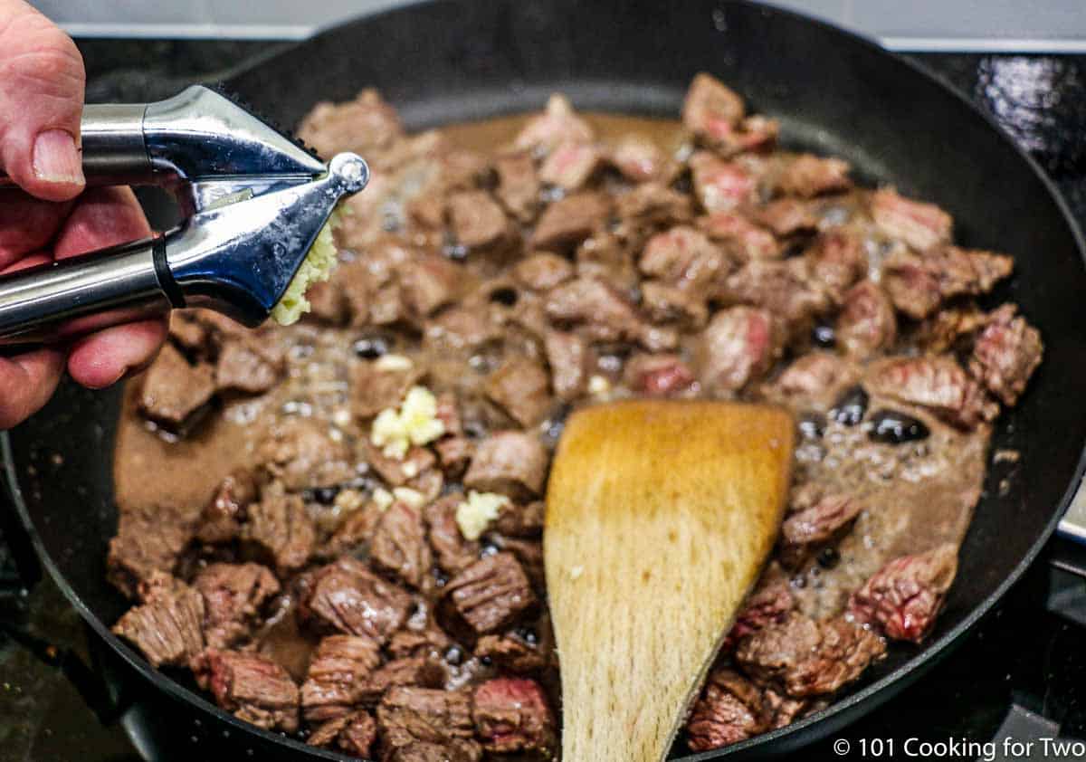 adding garlic to browning meat in a black skillet
