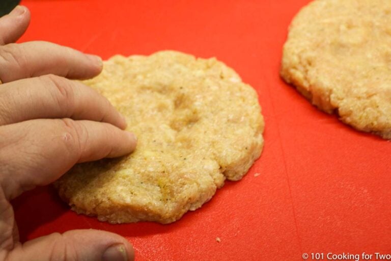 ground chicken patties with a dimple on a red mat.