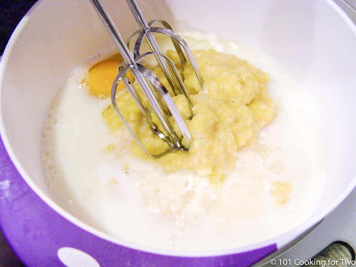 mixing ingredients in a white bowl with a hand mixer.