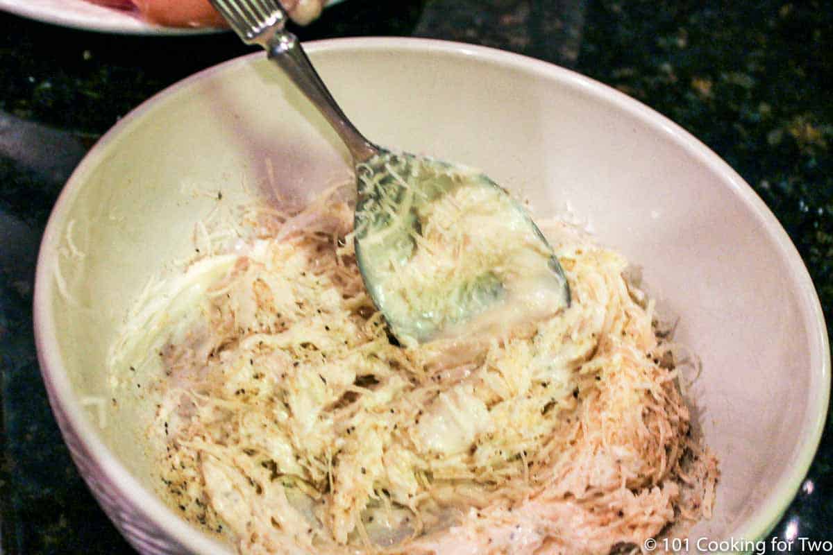 mixing mayo with Parmesan and spices in white bowl.