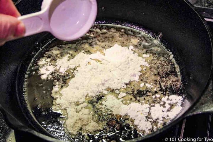 adding flour to fat in black pan