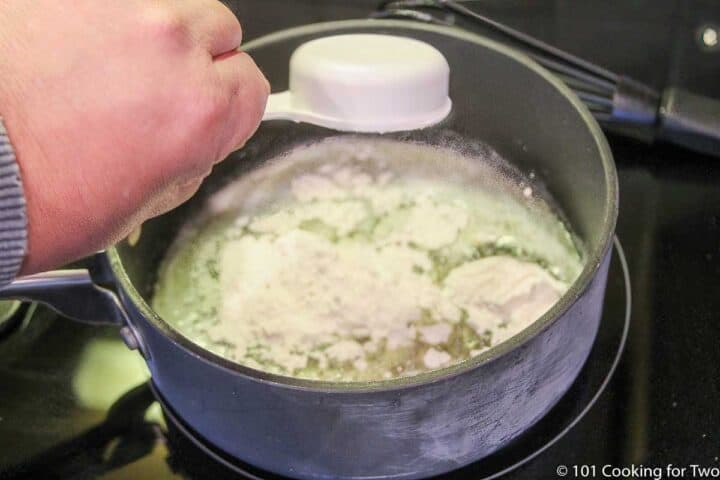 adding flour to melted butter in a black sauce pan