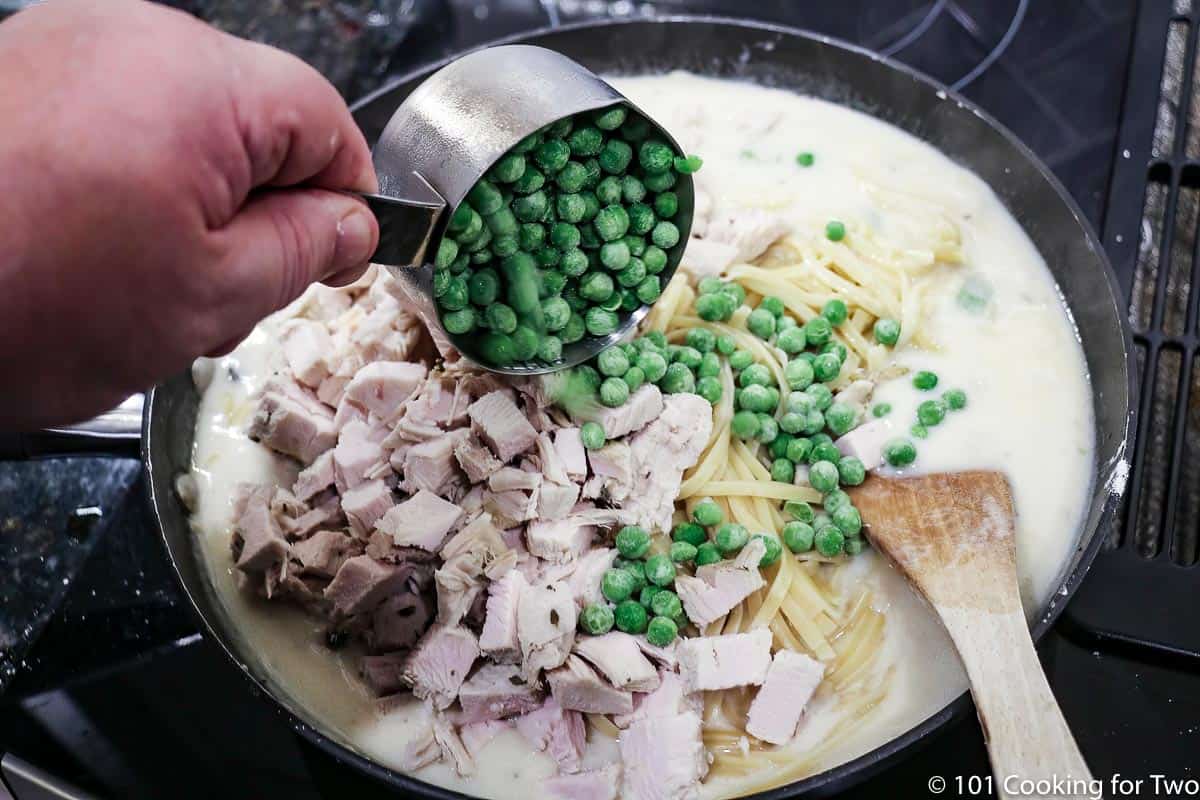 adding turkey cubes and frozen peas to the sauce with pasta