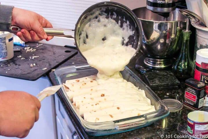pouring sour cream sauce over the dish of enchiladas