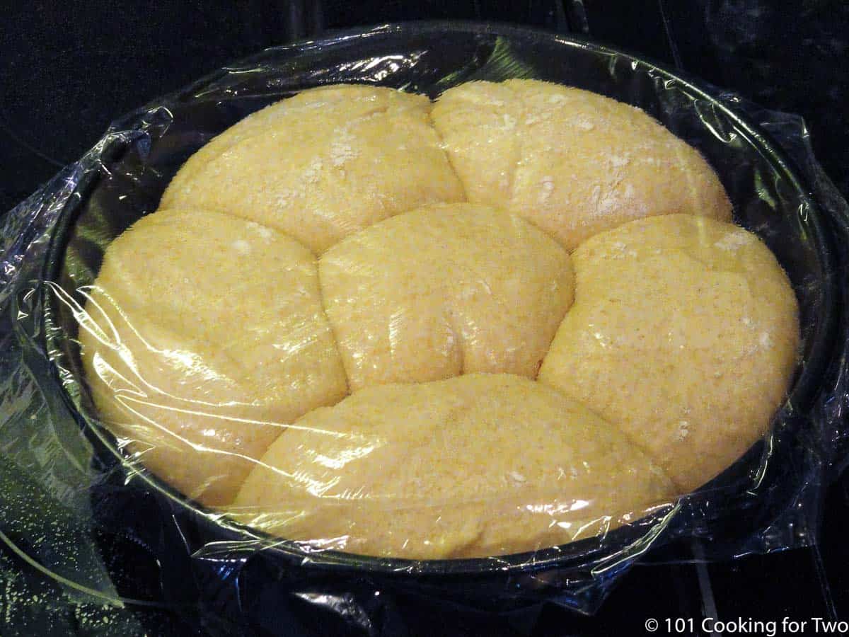 raised wheat rolls in pan covered with plastic wrap.