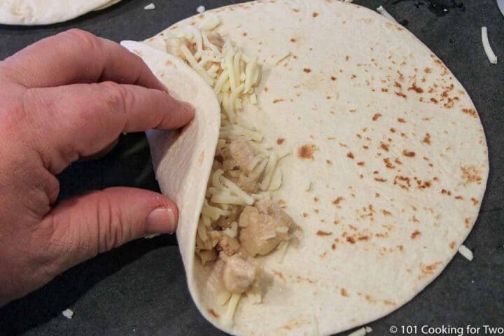 rolling chicken mixture and cheese in tortilla