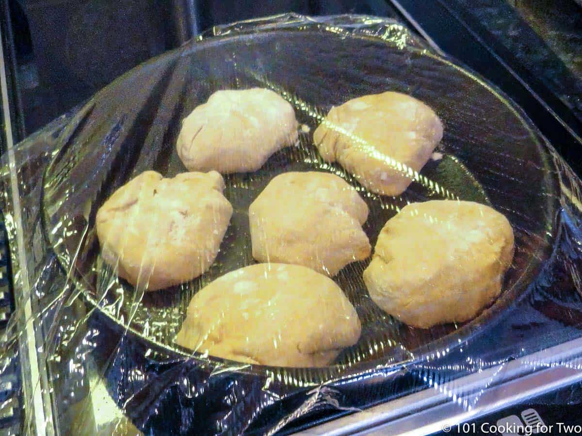 six pieces of dough in a round baking pan with plastic wrap.