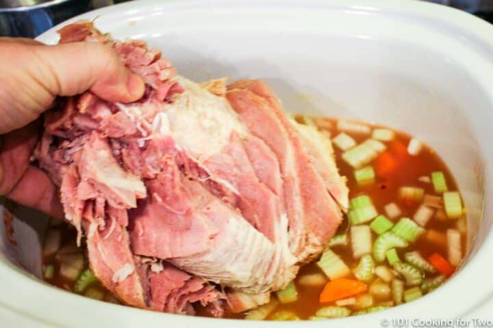 adding meaty ham bone to crock pot with borth and vegetables