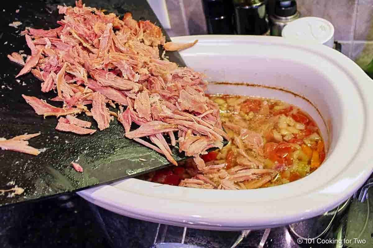 Adding shredded ham into the crock pot.