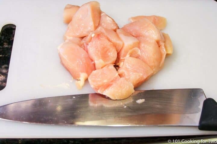 chicken cut into cubes on a white board with a knife