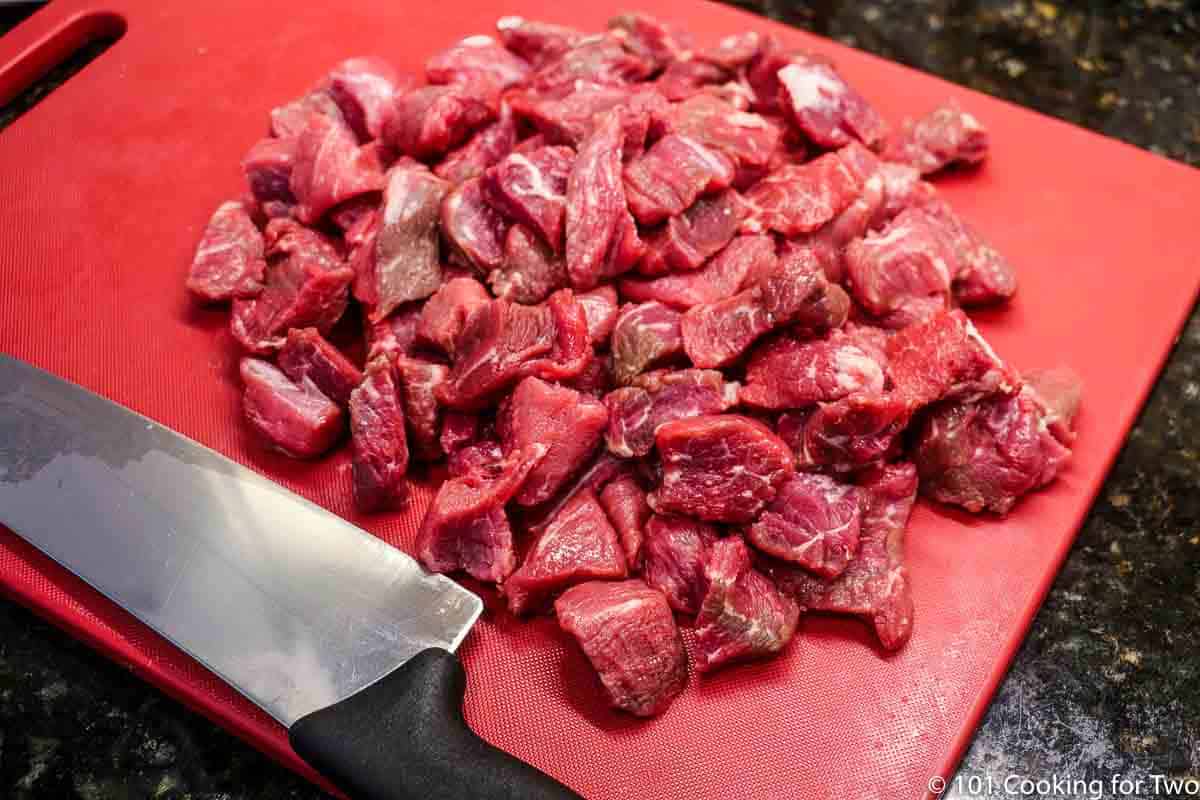 chunks of beef on a red board with a knife