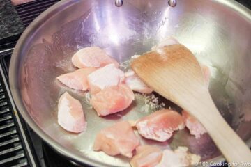 cooking raw chicken in a pan with a wooden spoon