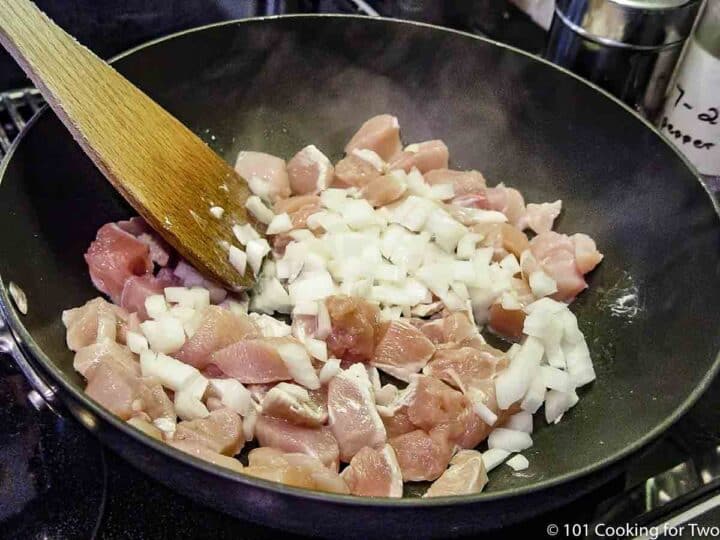 cooking raw chickenh with onion in a black pan