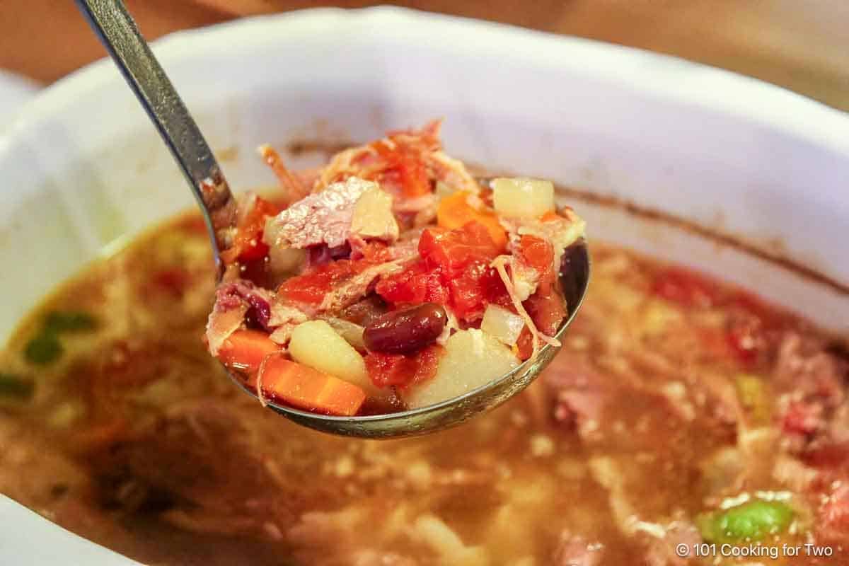 Ham and vegetable soup in a ladle.