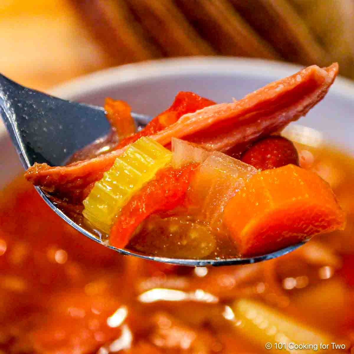 Ham and vegetable soup on a spoon.