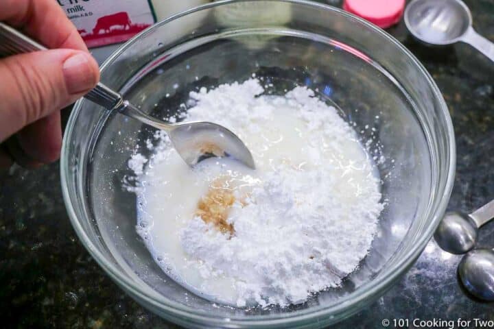 mixing powdered sugar with milk and vanilla in small bowl