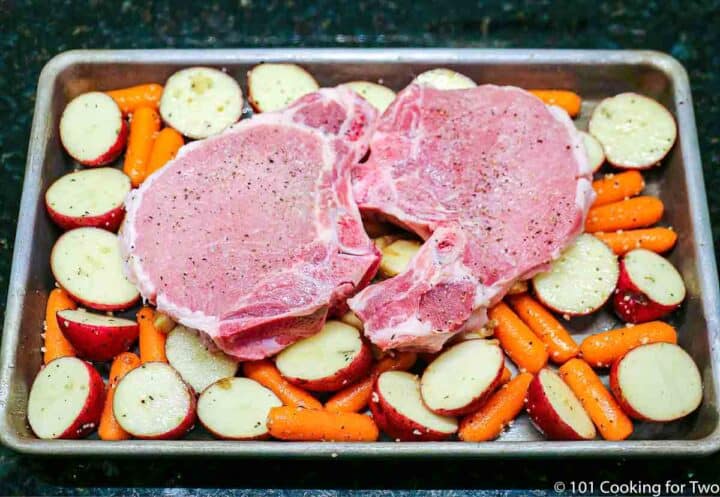 pork chops on top of apples and vegetables ready for the oven